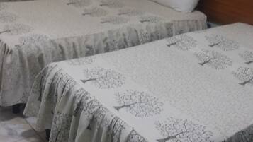 A bedroom with two beds, each with a patterned bedspread and a white pillow. There is a wooden headboard on one bed, and a small bedside table with a lamp.