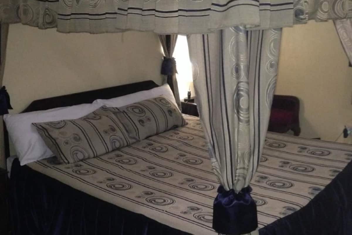 A four-poster bed with a canopy, a bedside table, and a lamp.