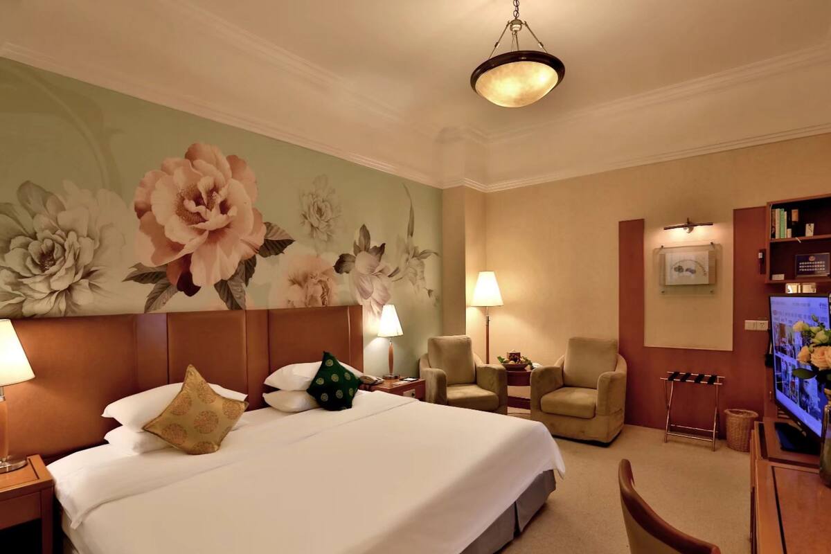 Ein Hotelzimmer mit einem großen Bett, zwei Sesseln, einem Schreibtisch mit Computer und einem Fernseher.