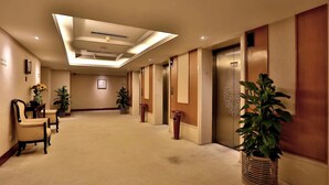 A hotel corridor with a carpeted floor, two chairs, potted plants, and an elevator. - Hangzhou Wenhua Jinglan Grand Hotel (Hangzhou)