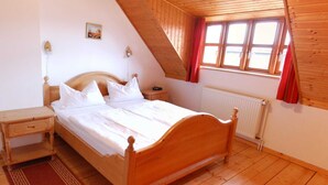 Un dormitorio con una cama de madera, una mesita de noche, un tapete rojo, una ventana con cortinas rojas y un techo de madera.