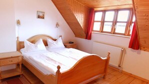 Un dormitorio con una cama de madera, una mesita de noche, un aparador, un radiador y una ventana con cortinas rojas.