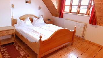 Ein Schlafzimmer mit einem hölzernen Bett, einem Nachttisch, einer Kommode, einem Heizkörper und einem Fenster mit roten Vorhängen.