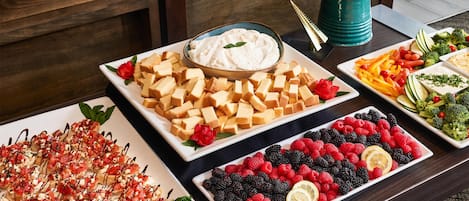 A table with various food items including cheese cubes, a fruit platter, and a bowl of dip.