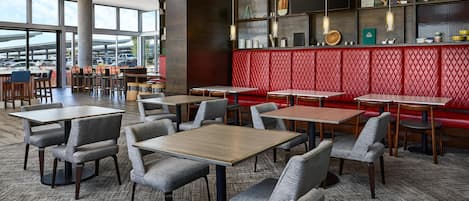 A modern restaurant with multiple tables and booths, a red cushioned seating area, and a large window offering a view of the parking lot.