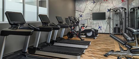 Un gimnasio con cintas de correr, bicicletas estáticas y equipo de levantamiento de pesas.