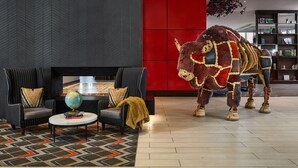 A modern lobby with a large bull statue, two armchairs with a globe and books, and a patterned rug. - Hyatt Place Peña Station/Denver Airport (Denver)