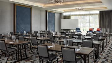 A conference room with multiple tables and chairs, a large screen, and a chandelier.