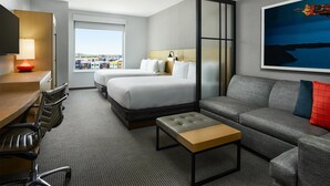 A modern hotel room with a bed, sofa, desk, chairs, and a city view. - Hyatt Place Peña Station/Denver Airport (Denver)