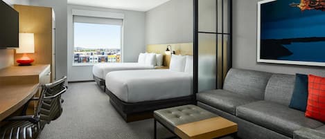 A modern hotel room with a bed, sofa, desk, chairs, and a city view.