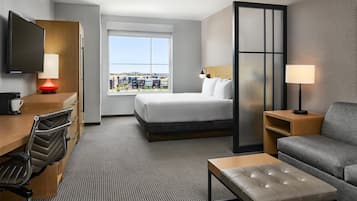 A hotel room with a bed, a desk, a chair, a sofa, a coffee table, and a TV.