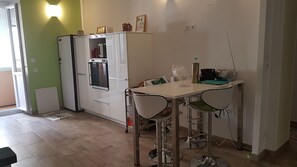 A compact kitchen with a white refrigerator, a microwave, and a small dining table with two chairs.