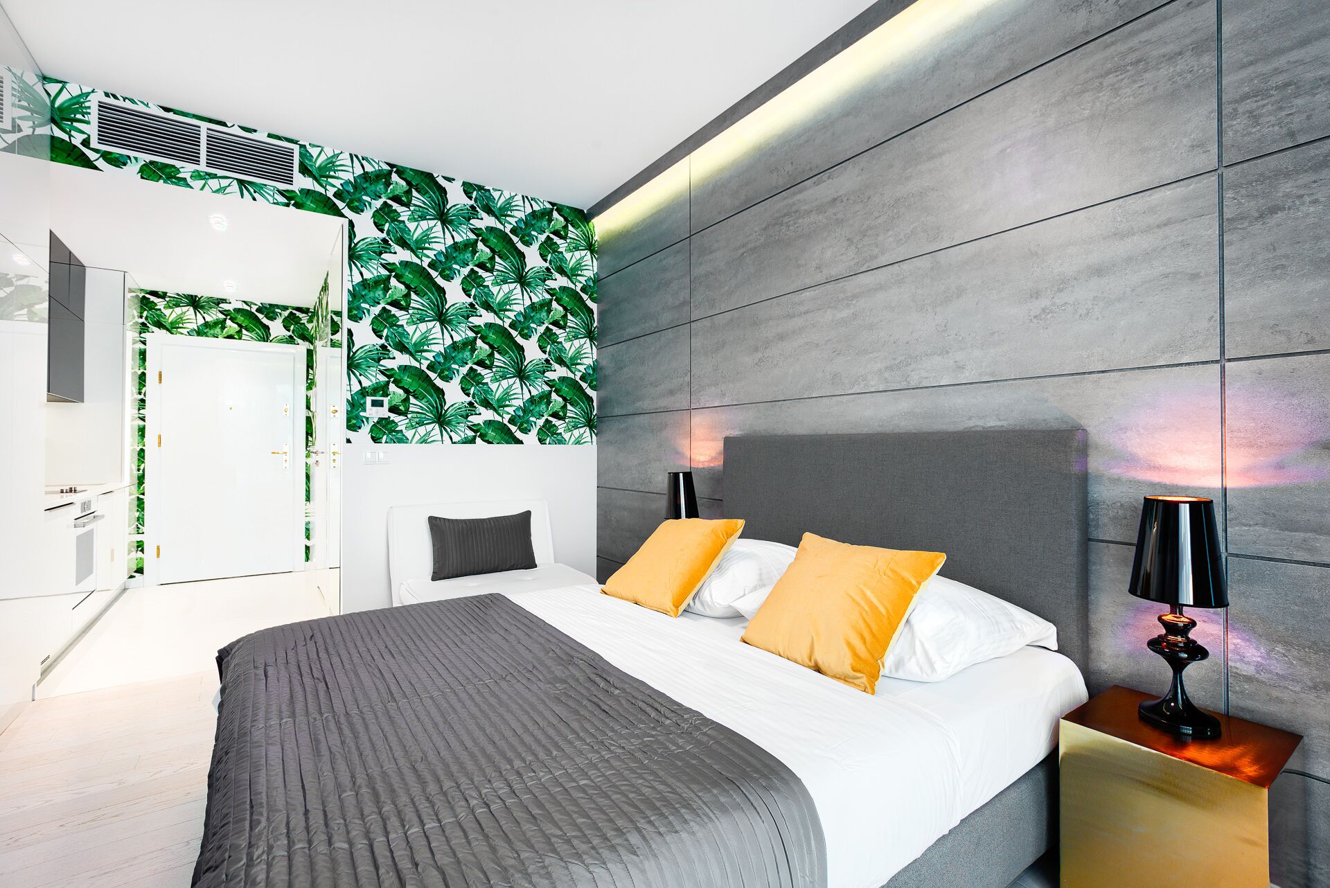 Une chambre moderne comprenant un lit, deux tables de chevet, une commode, une armoire et un mur orné d’un motif de feuilles.