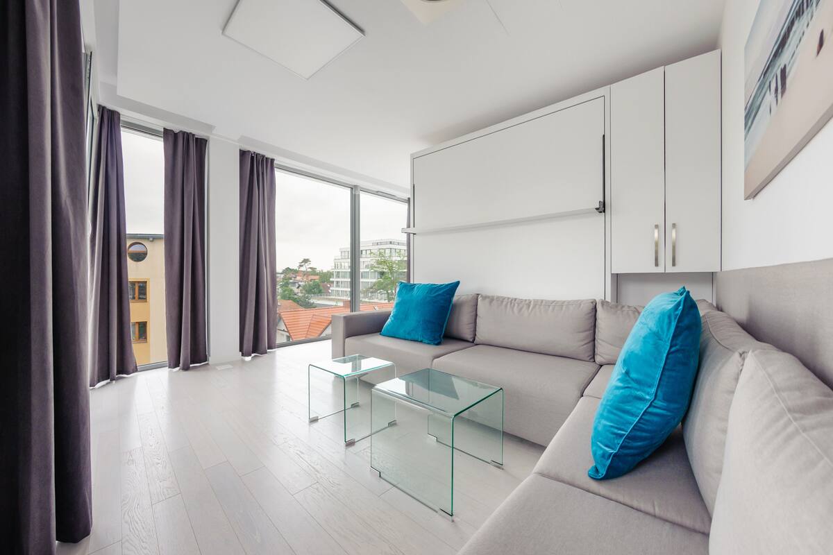 A modern living room with a sofa, two glass coffee tables, and a view of a cityscape through large windows.