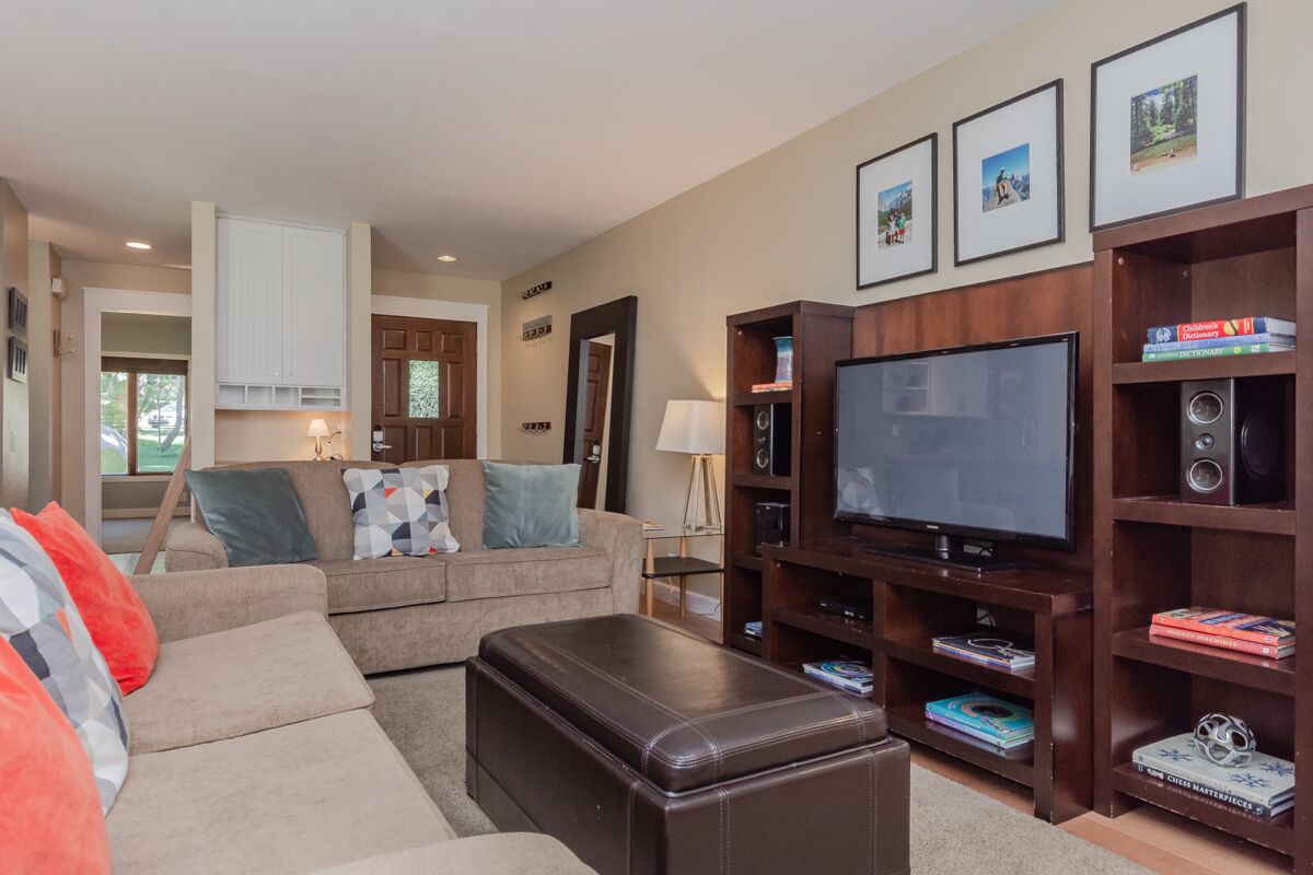 A living room with a sofa, ottoman, TV, bookshelf, and framed pictures on the wall.