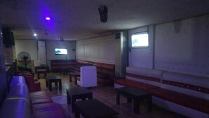 Un salon faiblement éclairé, avec des canapés, des tables et un écran de télévision.