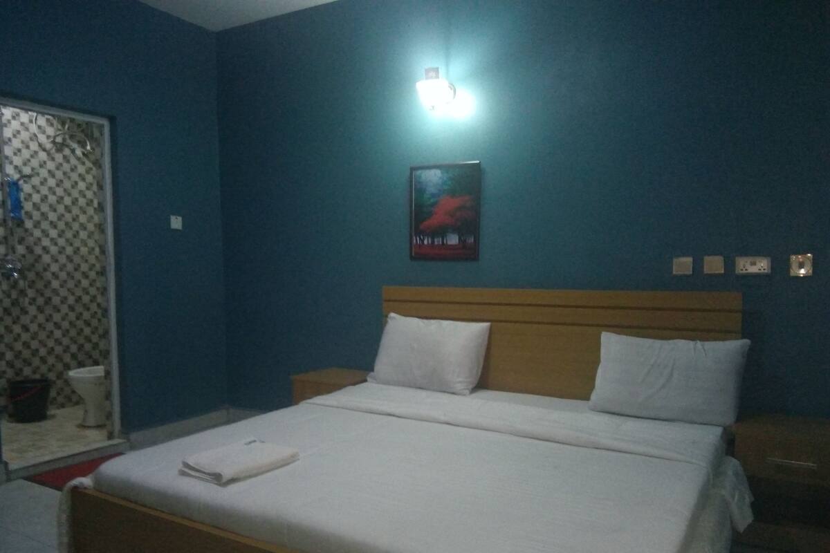 Een slaapkamer met een bed, een nachtkastje, een wandlamp en een poster.