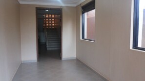 A corridor with a staircase leading to a landing, a window on the right, and a door at the end. - Rest Gardens (Kampala)