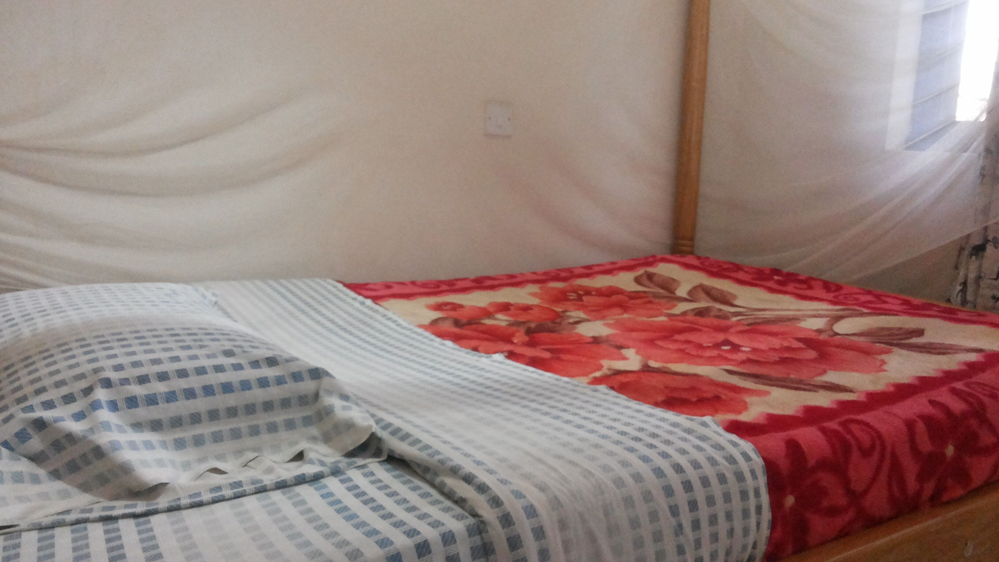 Una cama con una colcha estampada con motivos florales, un cojín a cuadros y una pared lisa con un enchufe.
