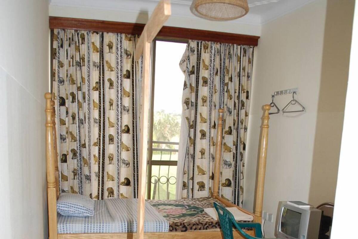 A room with two wooden beds, a desk, a chair, a television, and curtains with animal prints.