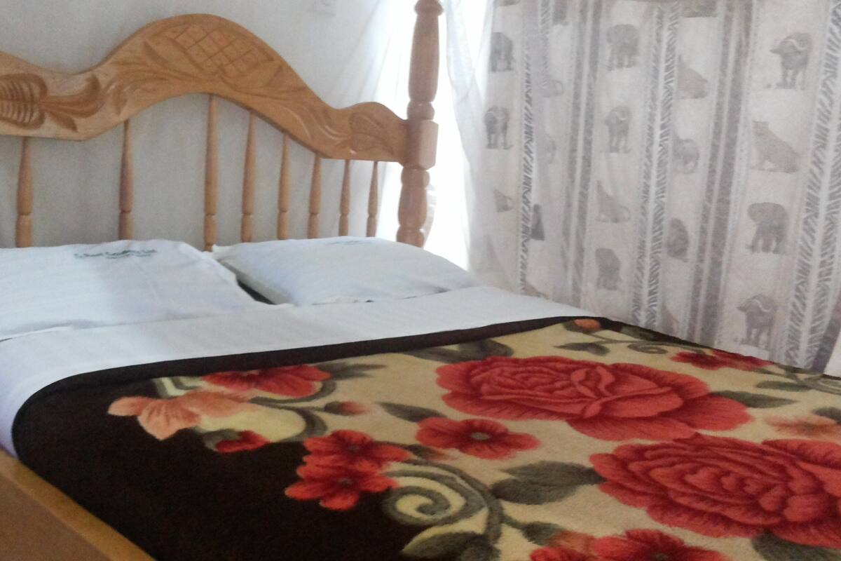 A bed with a wooden headboard, white bedding, and a floral-patterned blanket.
