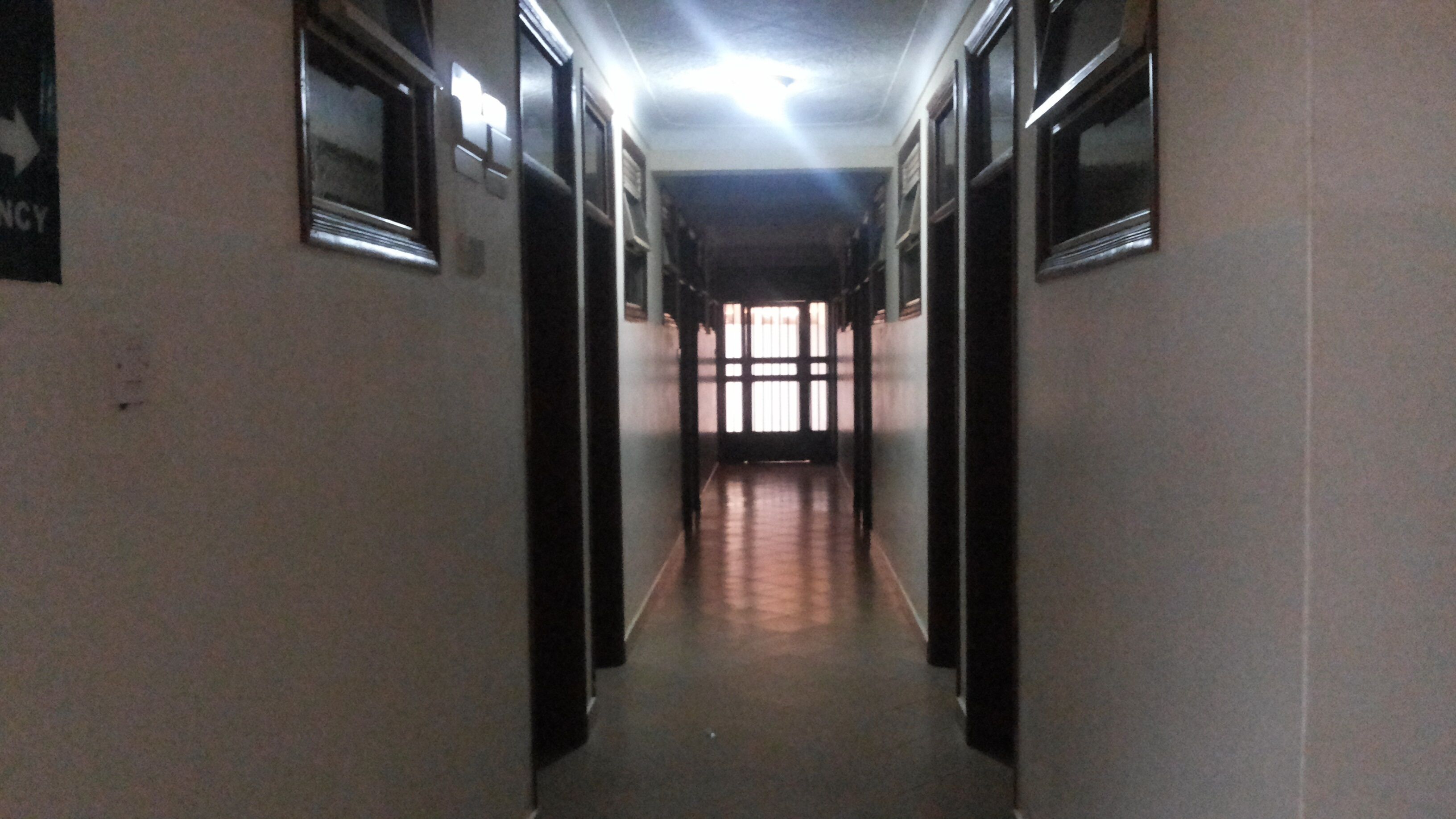 A long, narrow hallway with doors on both sides, leading to a bright room at the end.