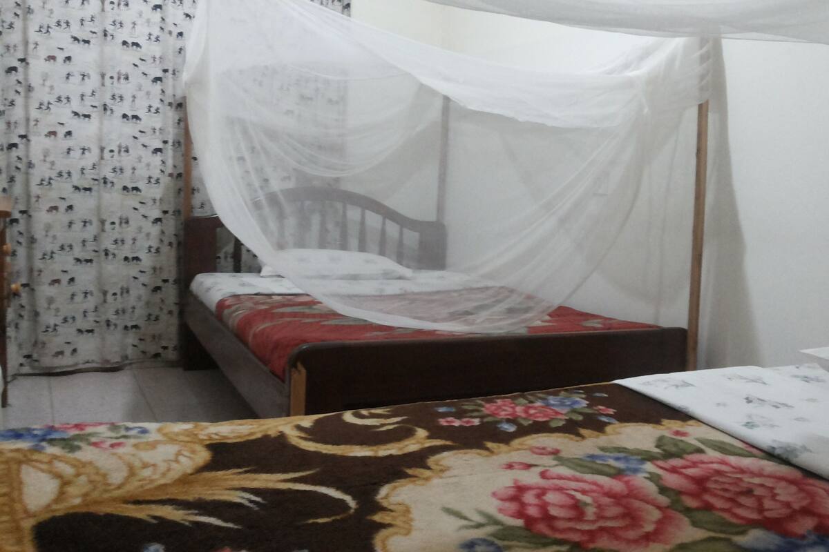 A bed with a mosquito net, a floral bedspread, and a patterned curtain.