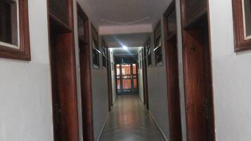 A long, narrow hallway with wooden doors on either side, leading to a brightly lit room at the end.