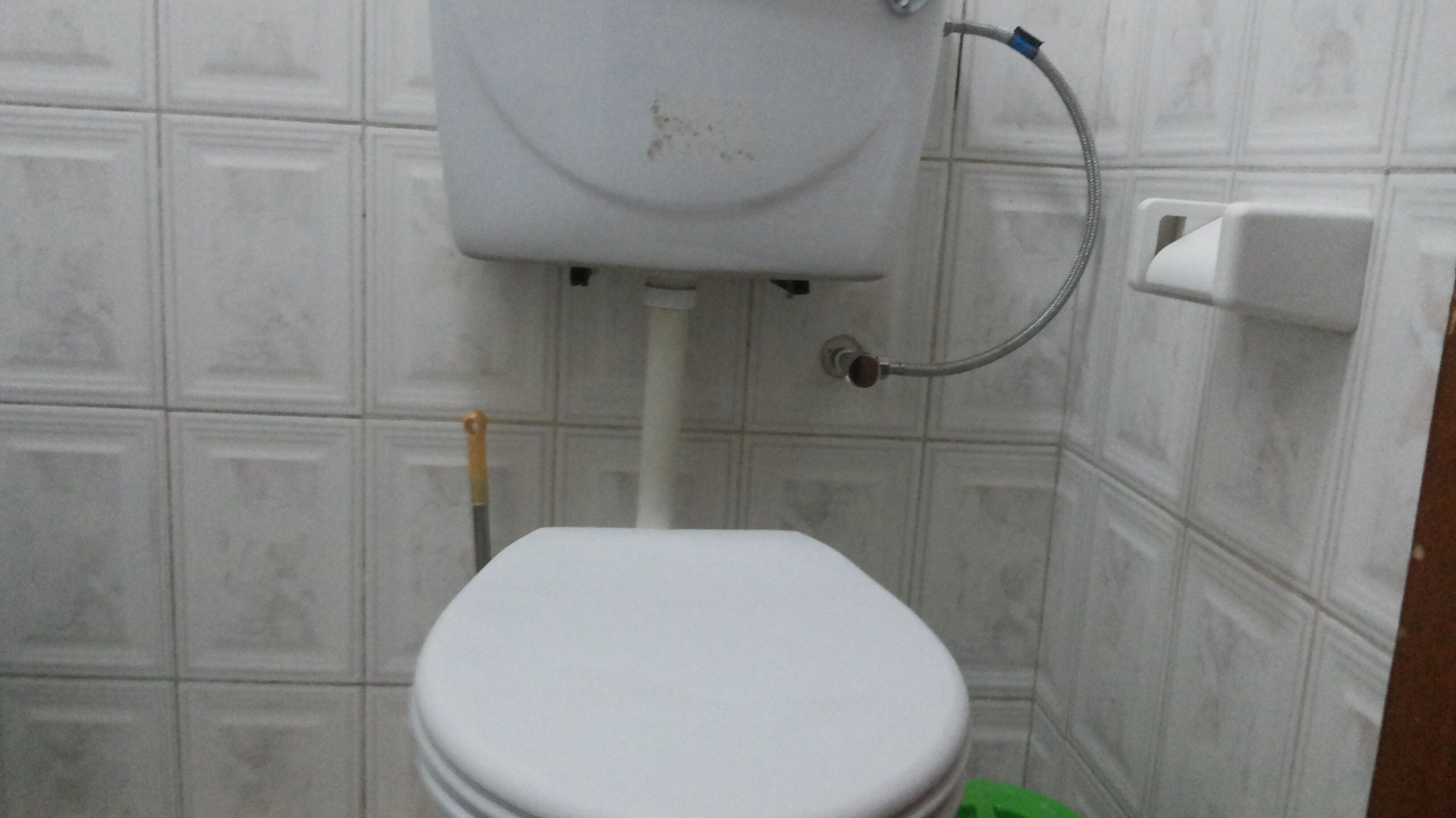 A bathroom with a white toilet, a visible pipe, and a wall-mounted flush handle.