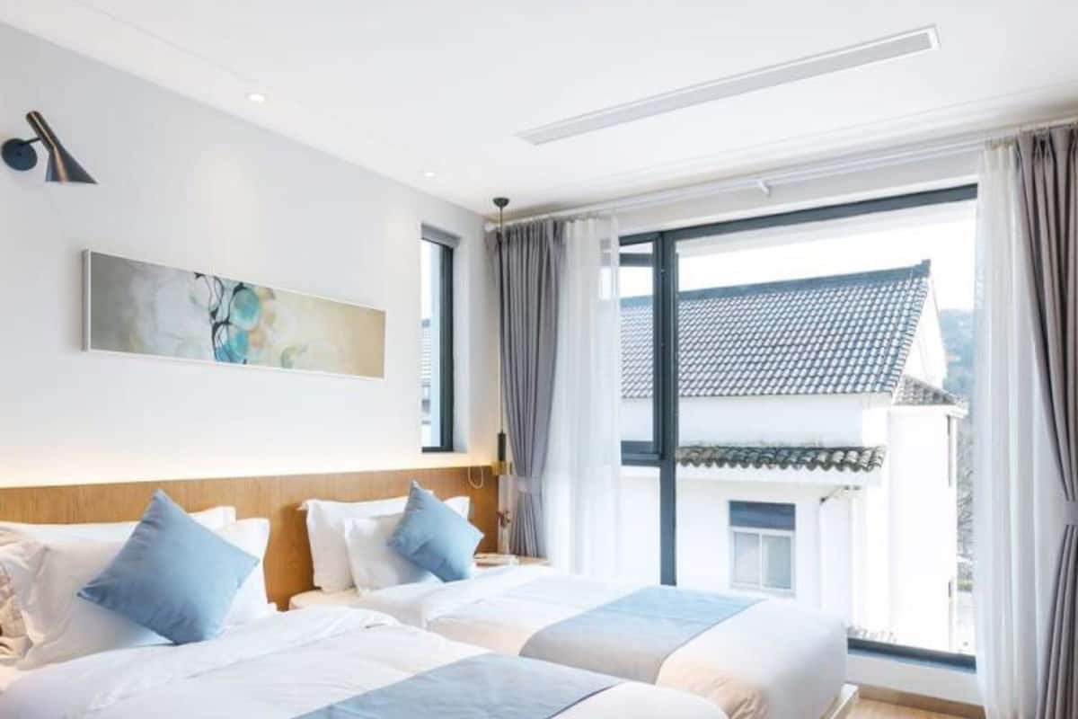 Habitación de hotel con dos camas, un ventanal con cortinas, una lámpara en el techo y un cuadro en la pared.