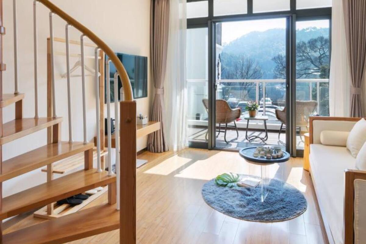 Una sala de estar moderna con una escalera de madera, un ventanal con vistas al exterior y una mesa de centro redonda.