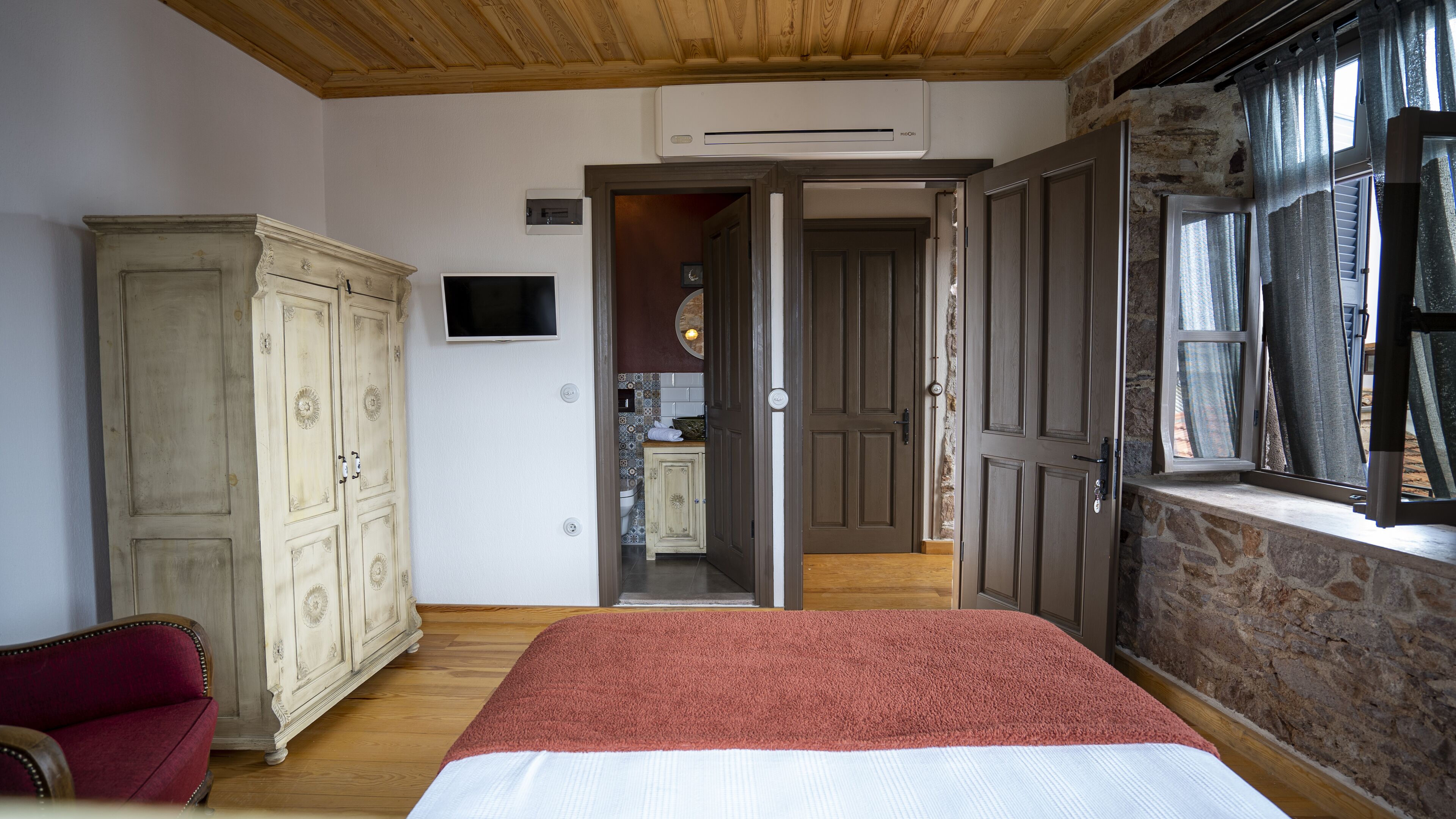Un dormitorio con techo de madera, una cama grande, un armario y vistas a una cocina a través de una puerta abierta.