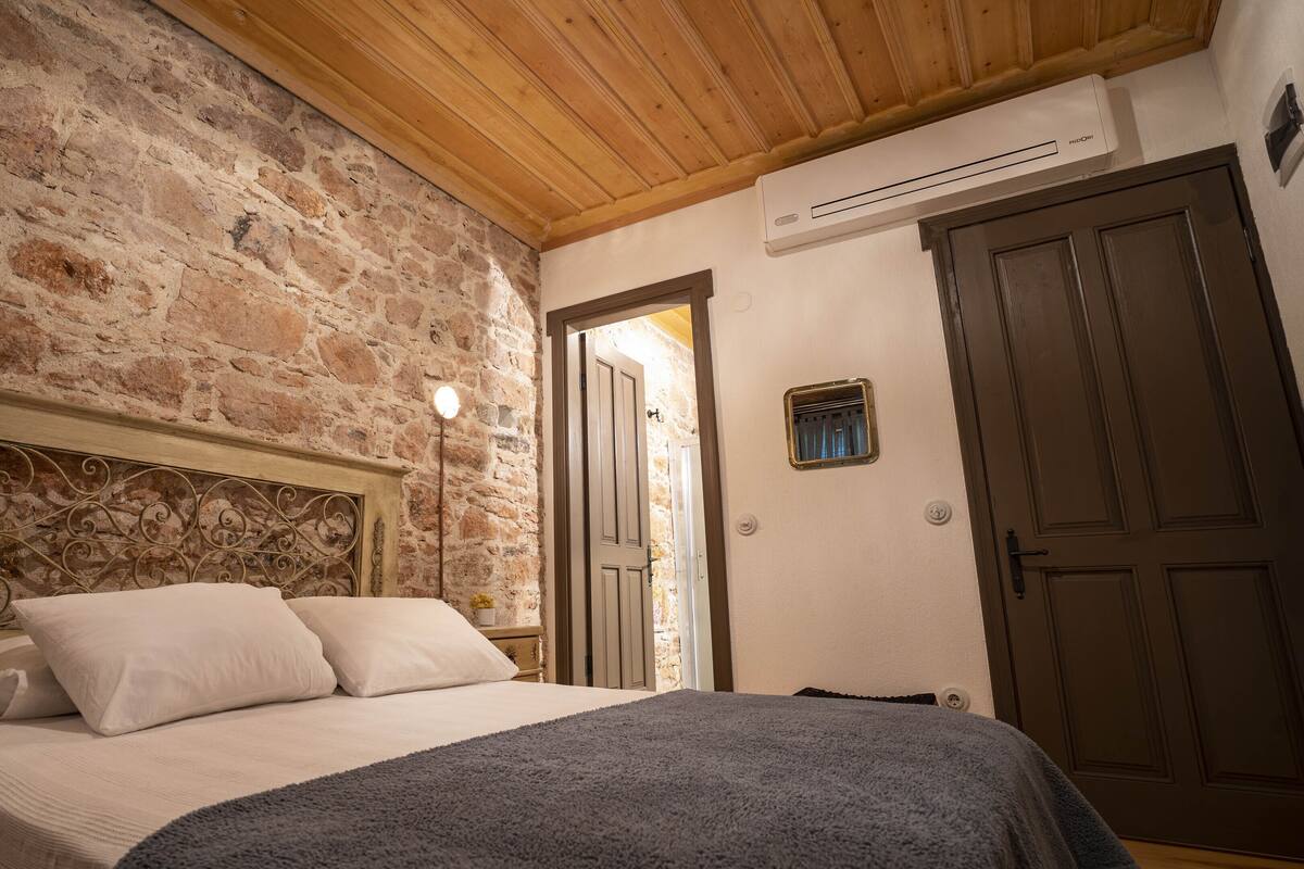 A bedroom with a stone wall, wooden ceiling, a bed with white bedding, and a wardrobe.