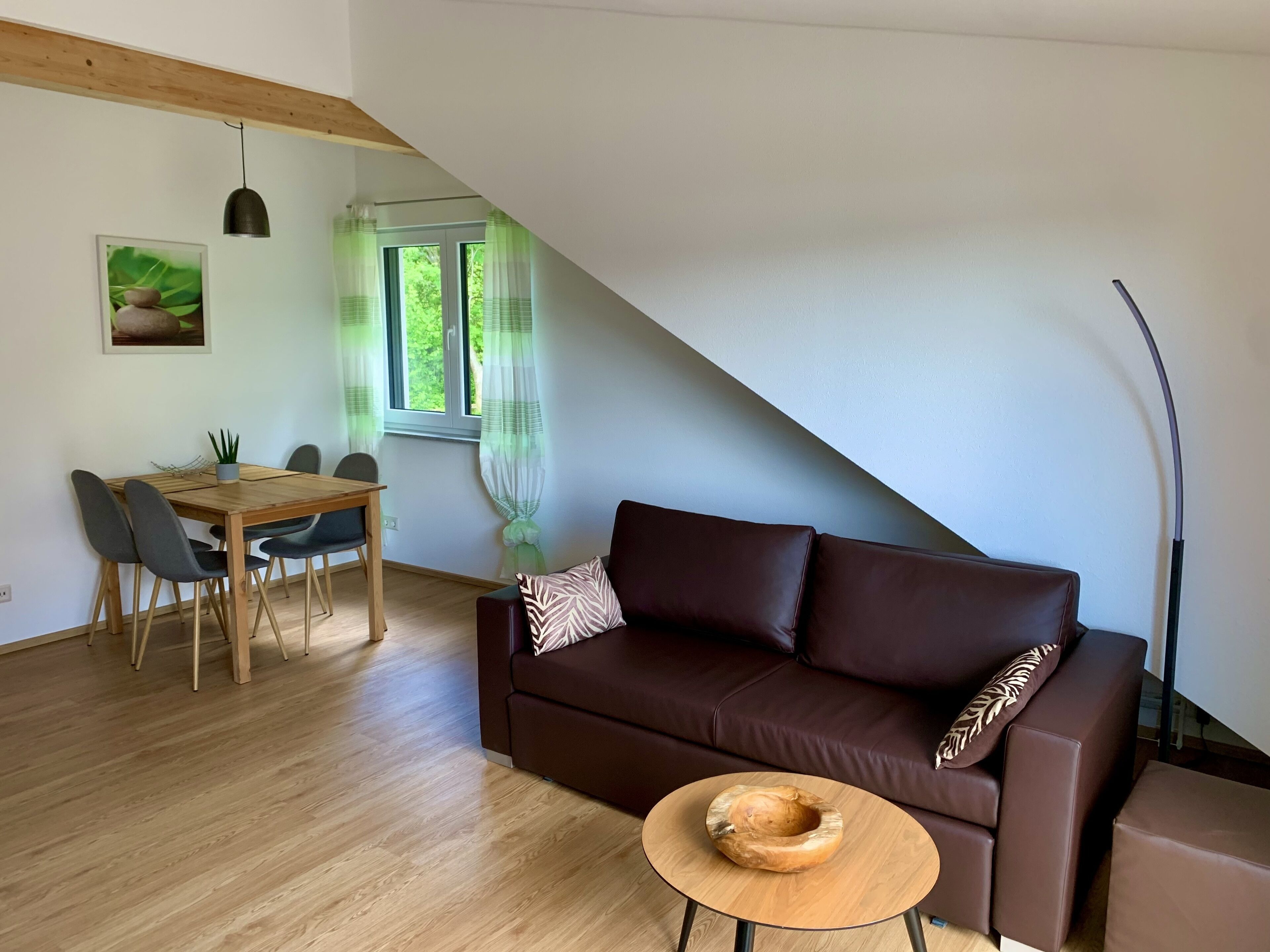 A modern living room with a brown leather sofa, a wooden dining table with chairs, and a small wooden side table.