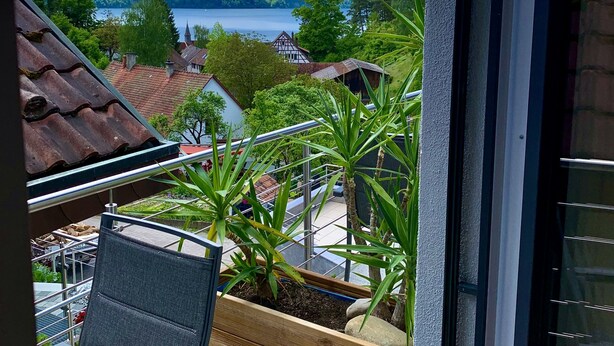 Ein Balkon mit Blick auf einen See, Häuser und Grünflächen.