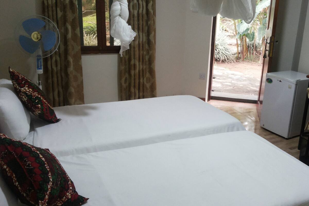 A room with two beds, a small desk, a chair, a fan, and a door leading outside.