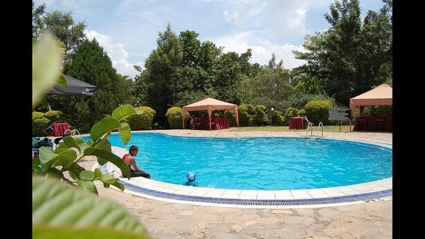 Una piscina con borde de azulejos, rodeada de suelo de piedra y toldos rojos.