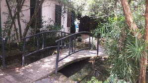 Un puente de piedra sobre un canal de agua, rodeado de vegetación y un edificio de fachada rosa.