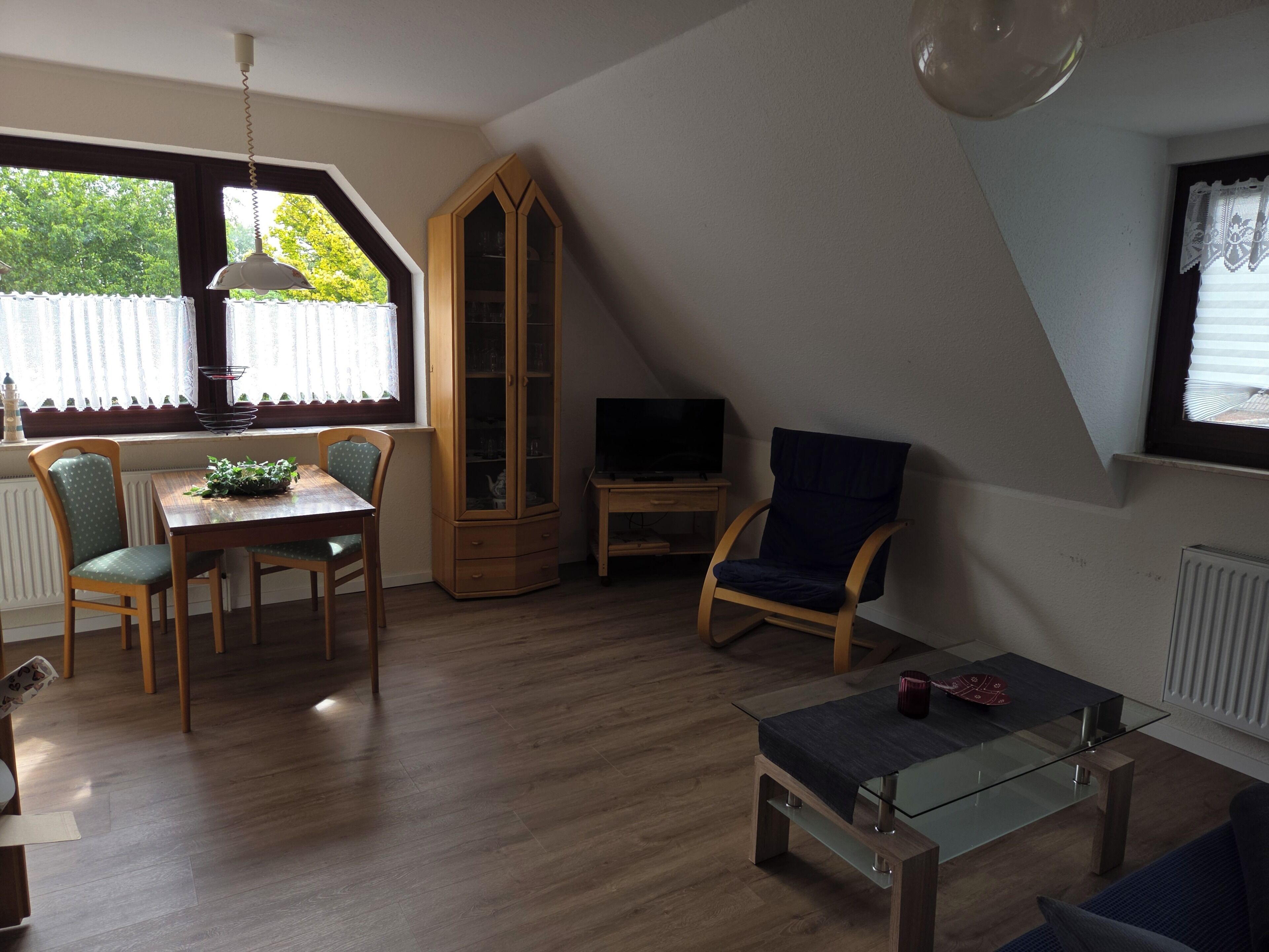 A room with a dining table, chairs, a cabinet, a television, and a glass coffee table.