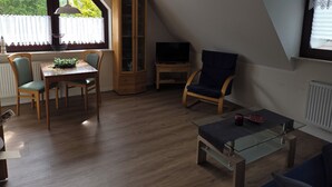 A room with a dining table, chairs, a cabinet, a television, and a glass coffee table. - Upper apartment in Westeraccum with balcony (Westeraccum)