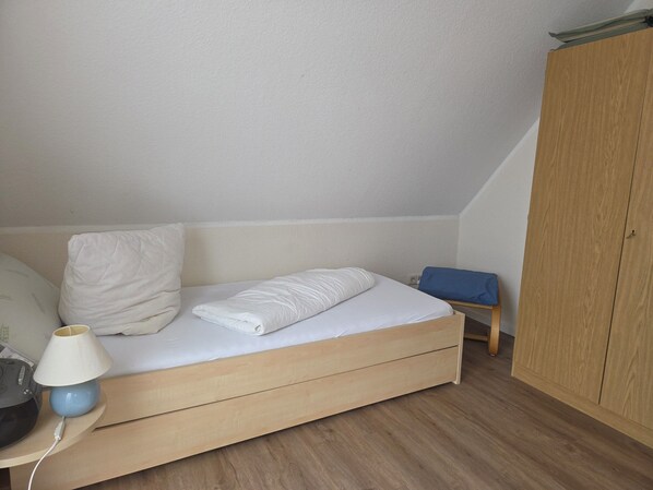 A bedroom with a wooden bed, a nightstand with a lamp, a chair, and a wardrobe. - Upper apartment in Westeraccum with balcony (Westeraccum)