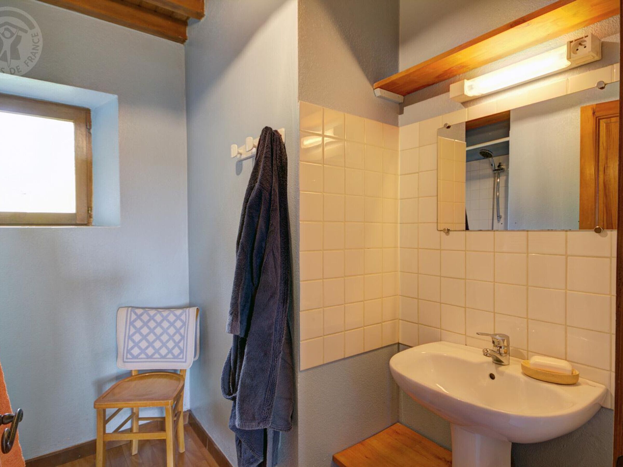 Ein Badezimmer mit einer Holzbank, einem Handtuchhalter, einem Waschbecken mit Seifenschale und einem Spiegel über dem Waschbecken.