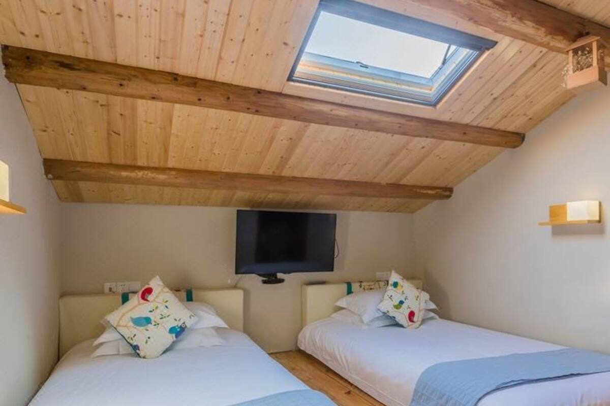 Un dormitorio con dos camas, un tragaluz, un televisor y vigas de madera.