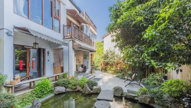 Edificio residencial con jardín que incluye un estanque, rocas y diversas plantas.