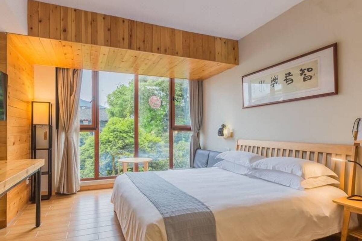 Un dormitorio con una cama grande, piso de madera, una ventana con cortinas, una mesita de noche y un cuadro enmarcado en la pared.
