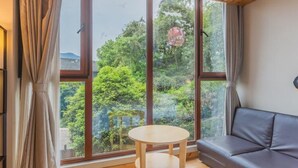 Una habitación con un ventanal grande, techo de madera, sofá, una mesita redonda y una cama.
