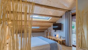 Un dormitorio con techo inclinado, una cama, un escritorio, un televisor y una ventana.