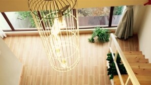 Un interior moderno con piso de madera, lámpara colgante, cojín blanco y una escalera.