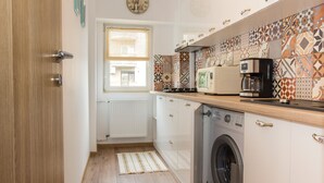 Une cuisine compacte équipée d’un lave-linge, d’une machine à café et d’une fenêtre avec des stores.