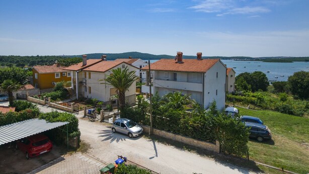 A residential area with houses, a parked car, and a body of water in the background. - Apartments Tara Apt 2 (Medulin)